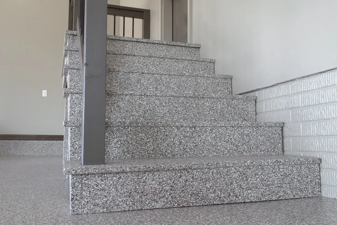Flight of stairs and landing coated in a gray and white flake finish beside a steel column