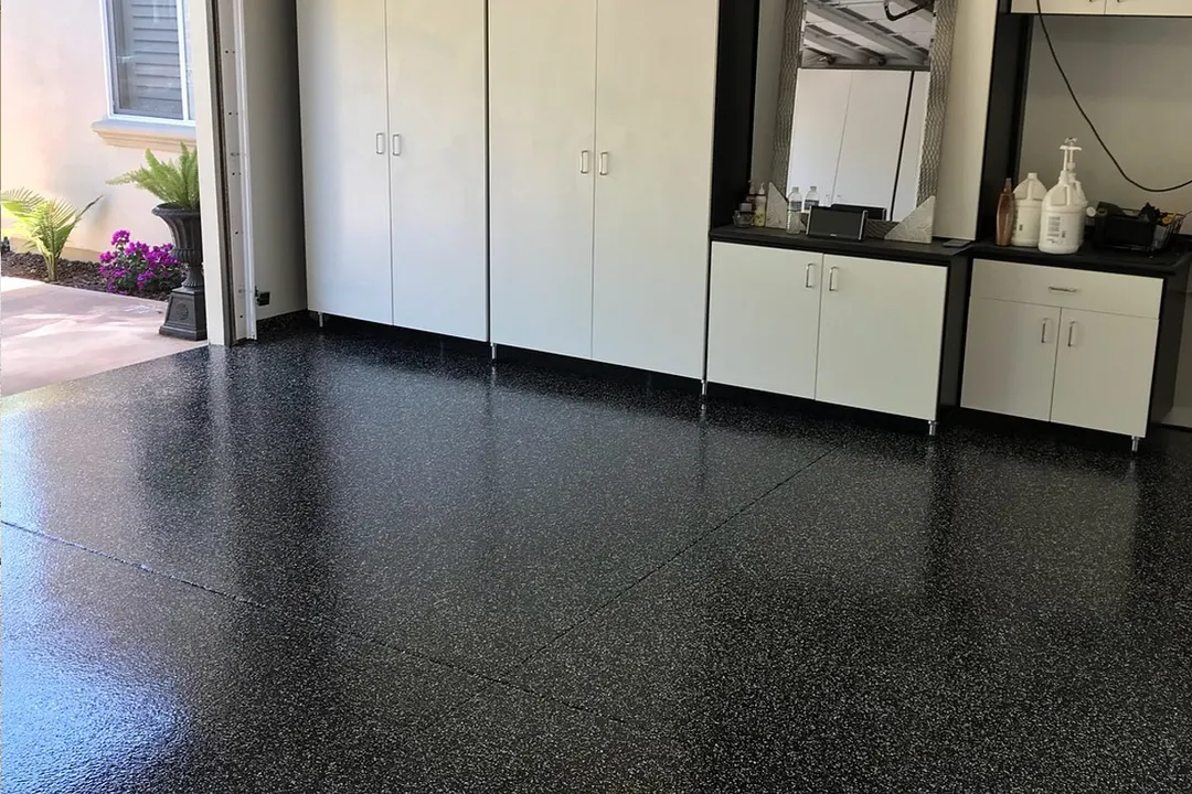Glossy black and white flake garage floor beside white cabinets with a black base