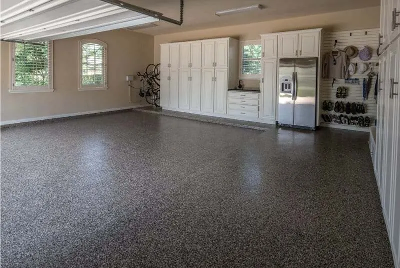 Dark brown and gray flake garage floor with white wall cabinets, a refrigerator and tool wall