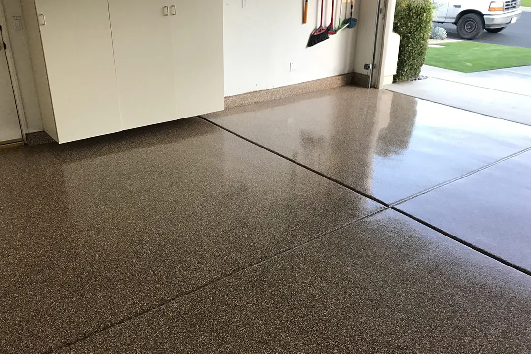 Glossy brown flake epoxy garage floor with a saw-cut joint and white cabinets along the wall