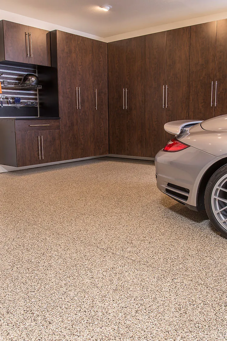 Beige and brown flake garage floor with dark wood-tone cabinets and a silver car