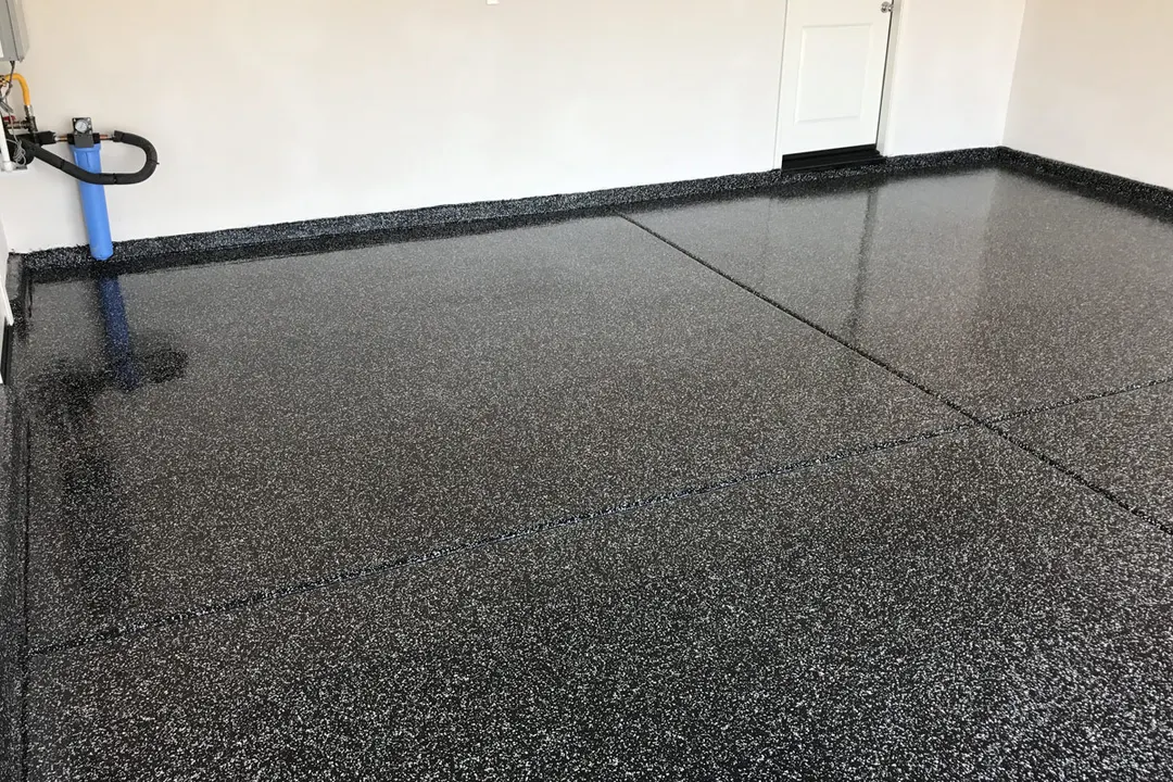 Dark charcoal and white flake floor meeting a white garage wall with a blue hose in the corner