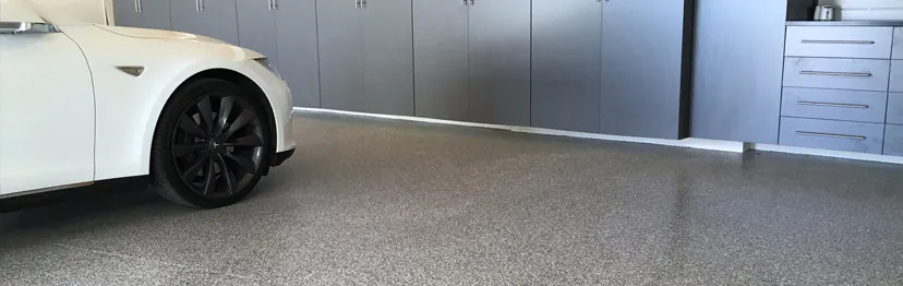 White car parked on a finished gray flake garage floor in front of gray storage cabinets