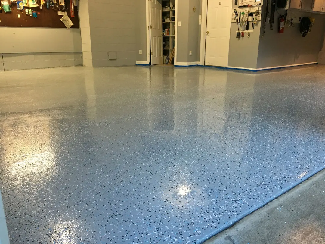 Glossy blue-gray flake garage floor reflecting light, with a workbench wall in the background
