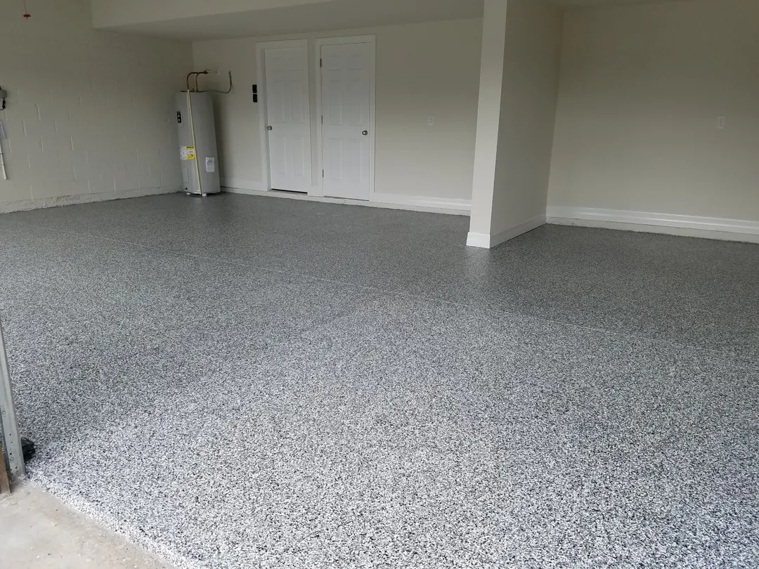 Empty garage with a gray and blue flake floor, a water heater and white doors