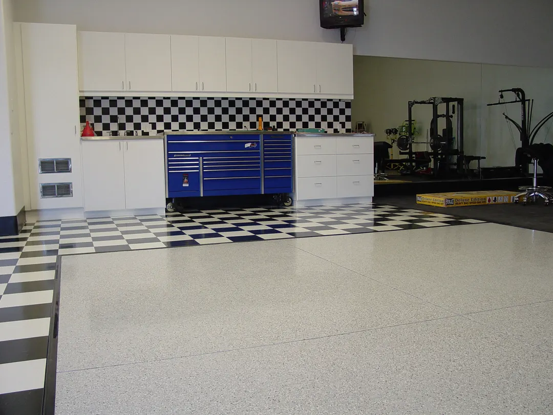 Garage workshop with a light flake floor, black and white checkered tile, white cabinets and a blue tool chest
