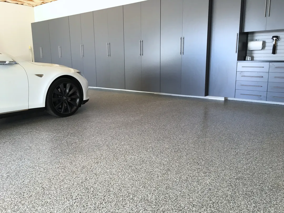 White car parked on a finished gray and white flake epoxy garage floor in front of charcoal storage cabinets
