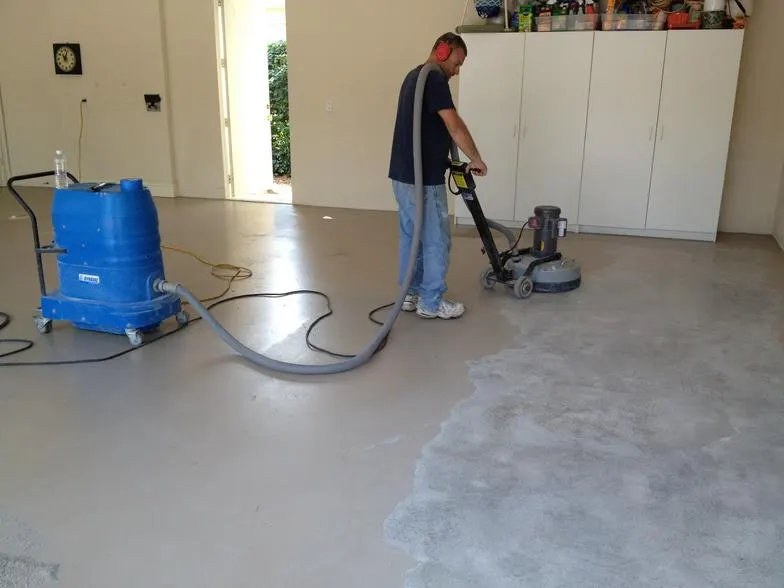 Technician using a floor grinder connected to a dust vacuum on a garage slab that is partly ground